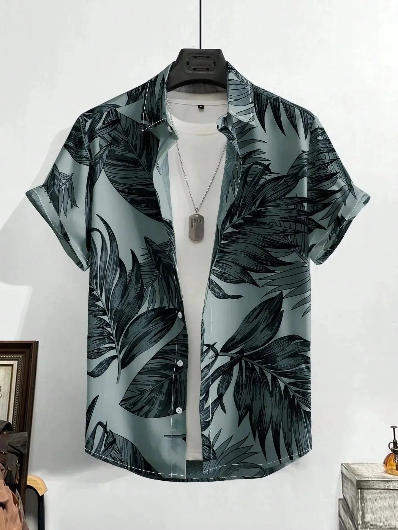Simples Market Hawaiian shirt with teal background and black tropical leaf print, short-sleeve on hanger