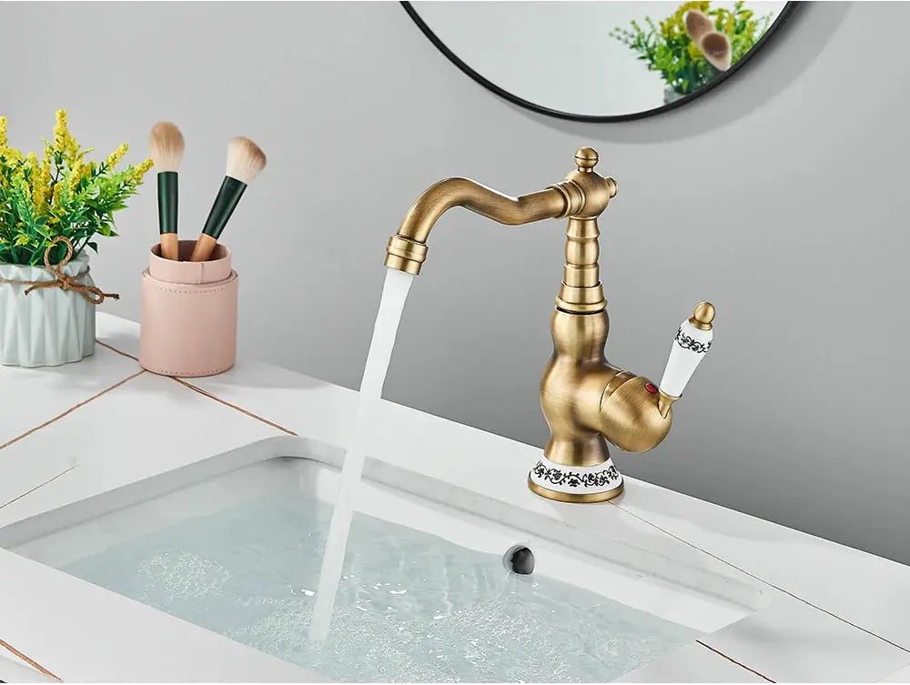 Antique brass bathroom faucet with rotating spout and white ceramic lever on a white sink.