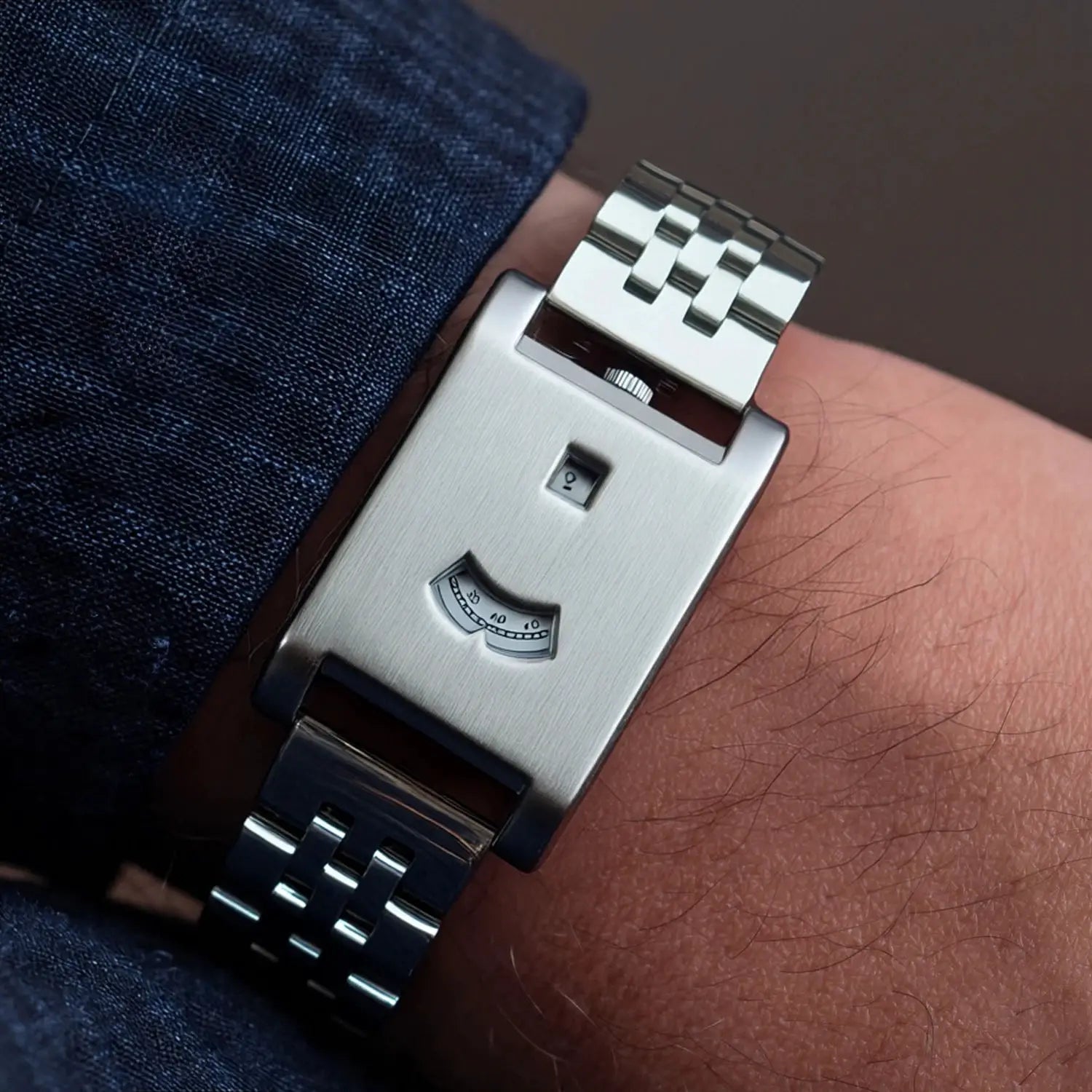 Men's square stainless steel tank watch with brushed finish and visible power-reserve gauge on the wrist