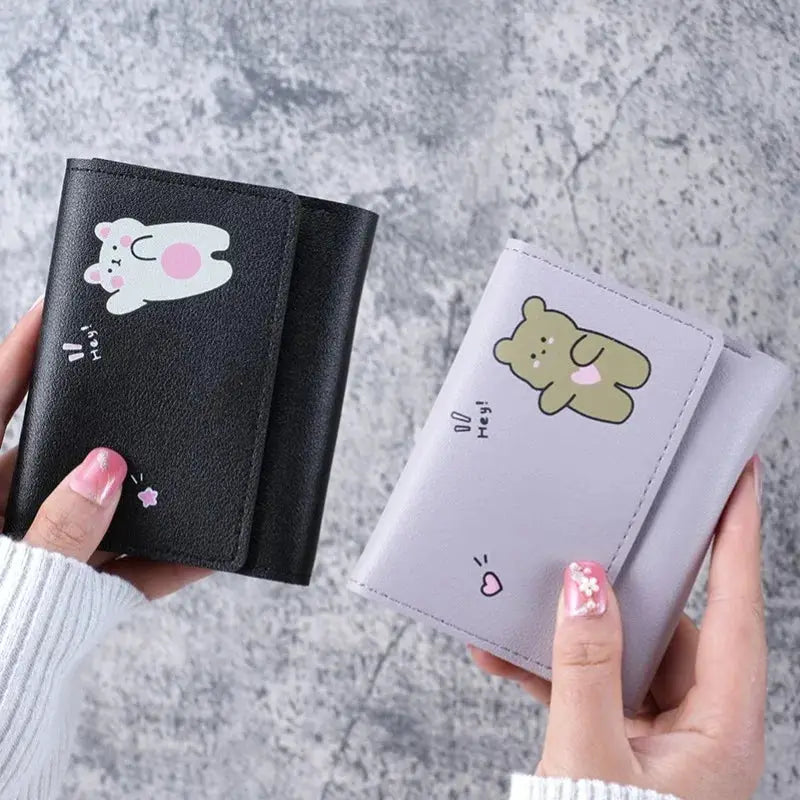 Two women's mini wallets with card slots and hasp closures, featuring black bunny and lavender bear cartoon designs