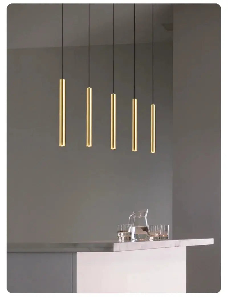 Minimalist pendant lights by Simples Market; five gold cylindrical LED lamps hanging over a kitchen island.