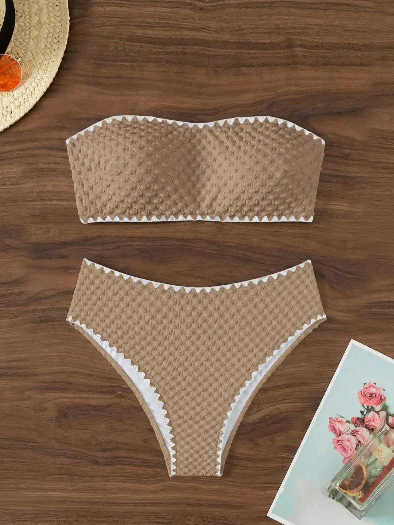 Beige textured two-piece strapless bandeau bikini with white trim on wooden surface
