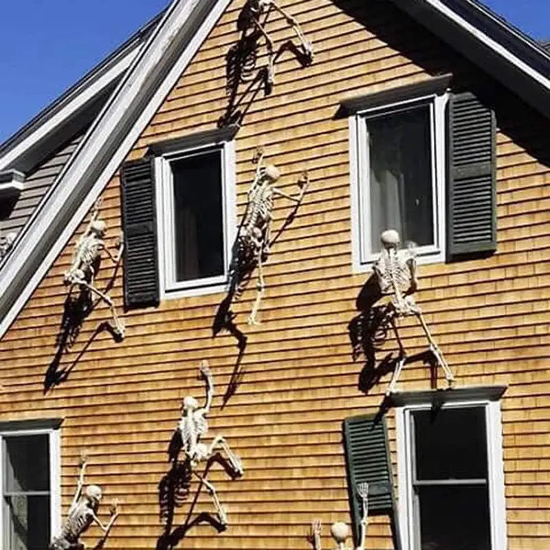 Happy Halloween humanoid skeleton prop; several bone-white skeletal figures climbing a wooden house exterior.