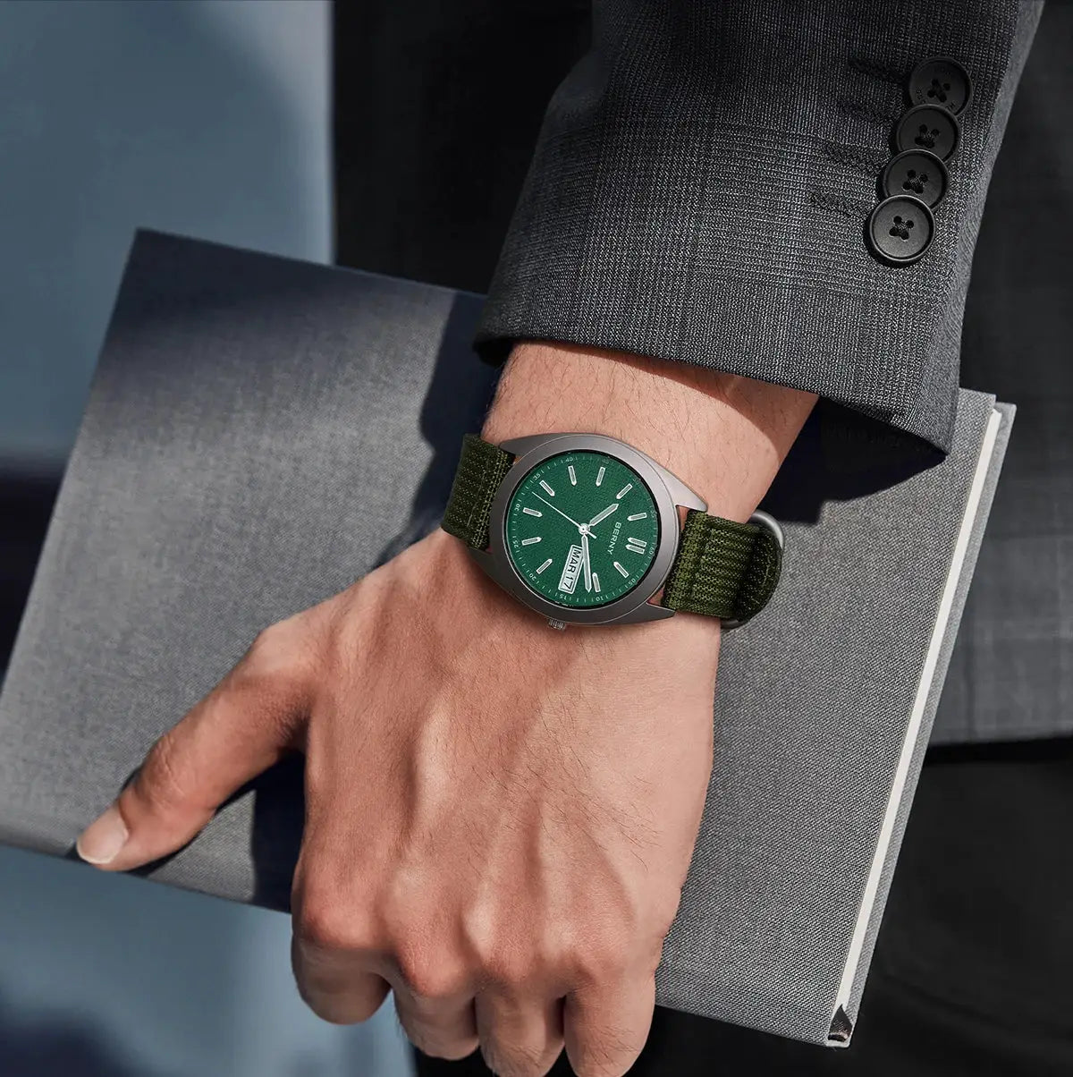 BERNY titanium men's watch with green dial and green fabric strap on a wrist beside a gray notebook