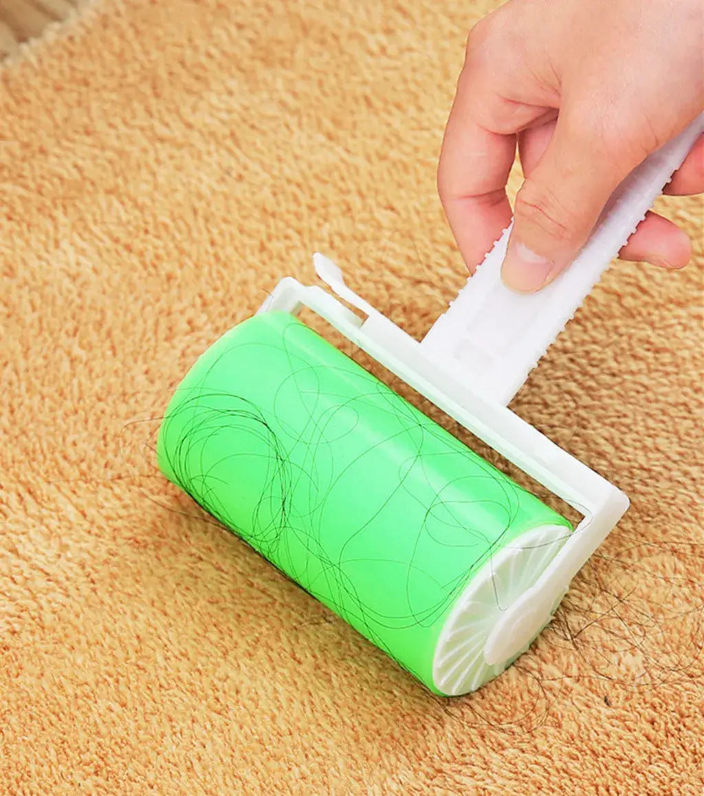 Green reusable sticky pet-hair roller with white frame on tan carpet; hand peeling off used adhesive sheet.