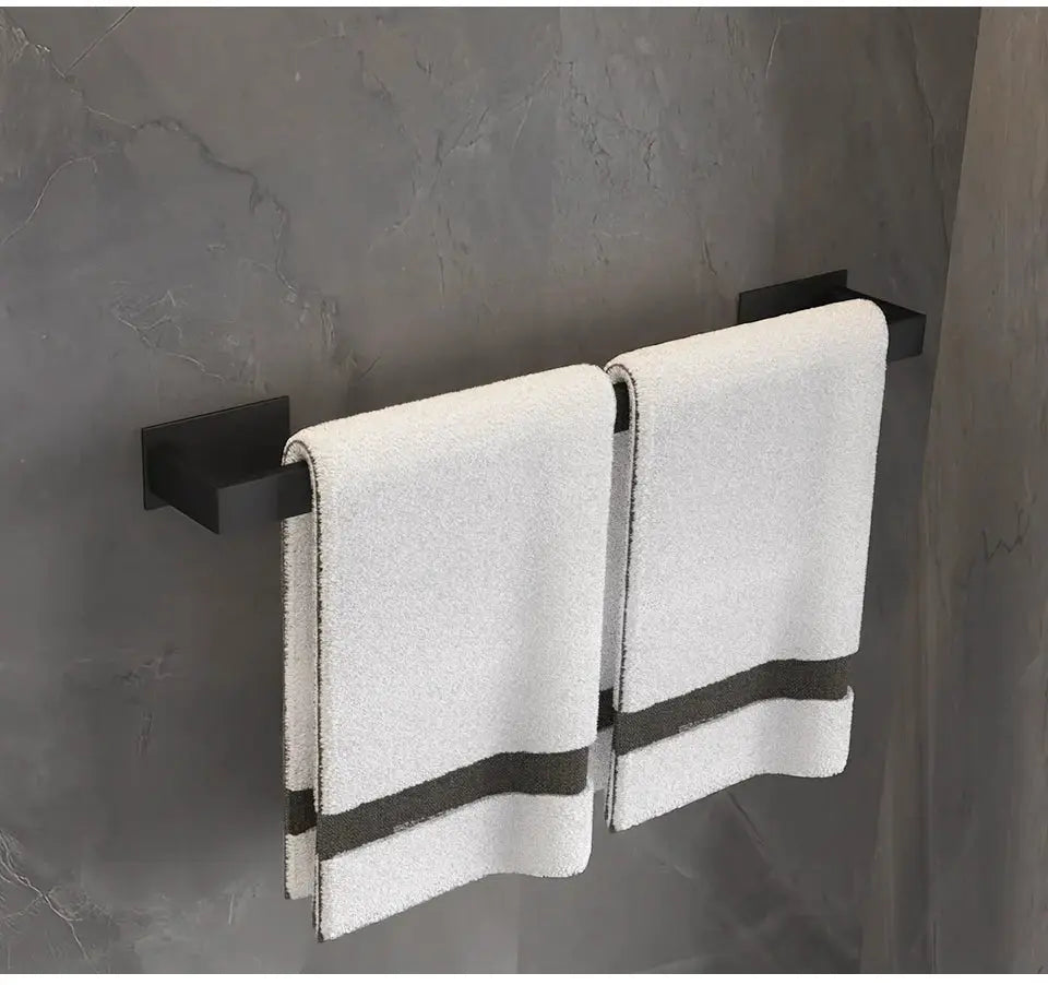 Black self-sticking towel rail set with two bars mounted on a gray wall, white towels hung