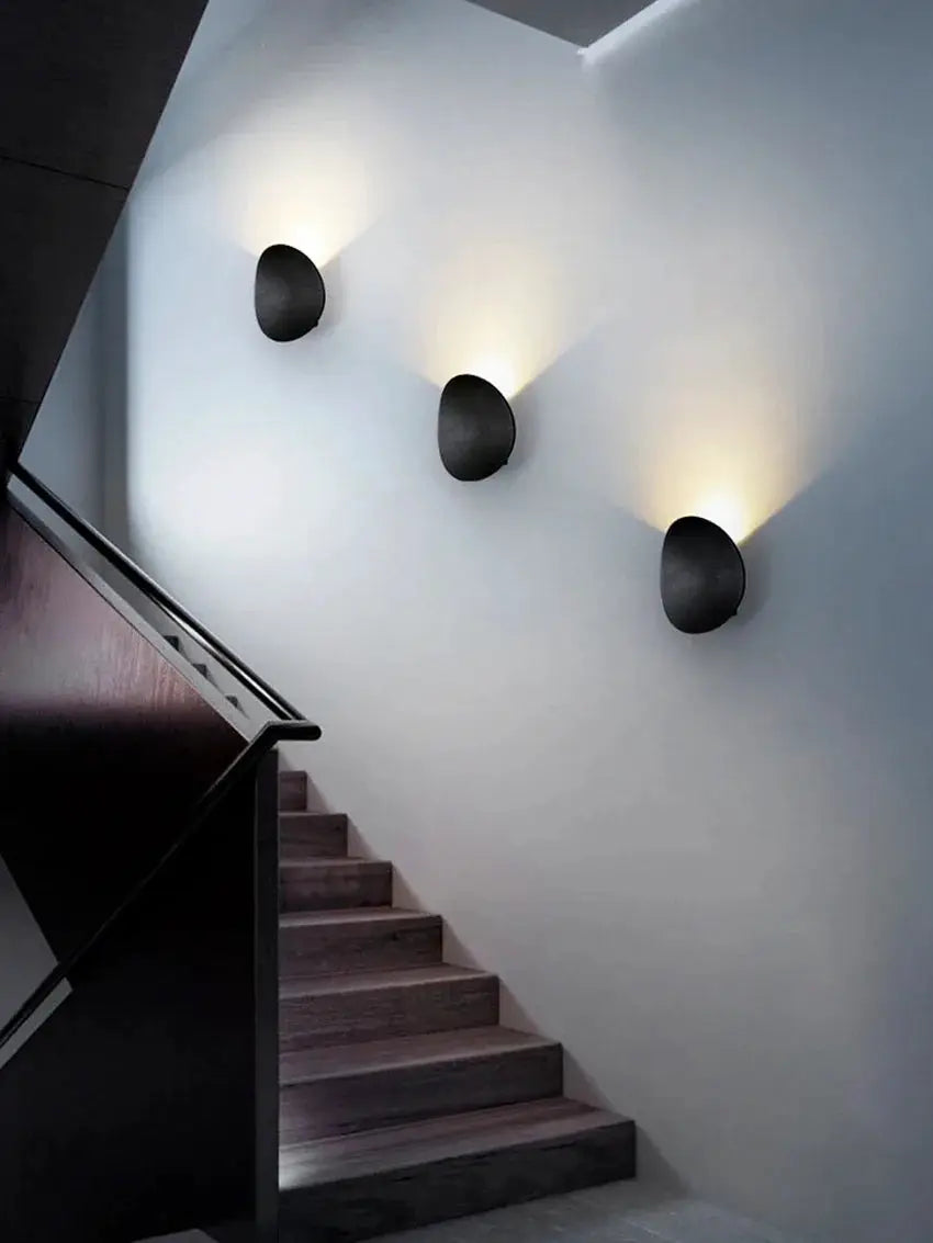 Outdoor LED wall lamp; three black round wall-mounted lights casting warm white glow along stairwell wall