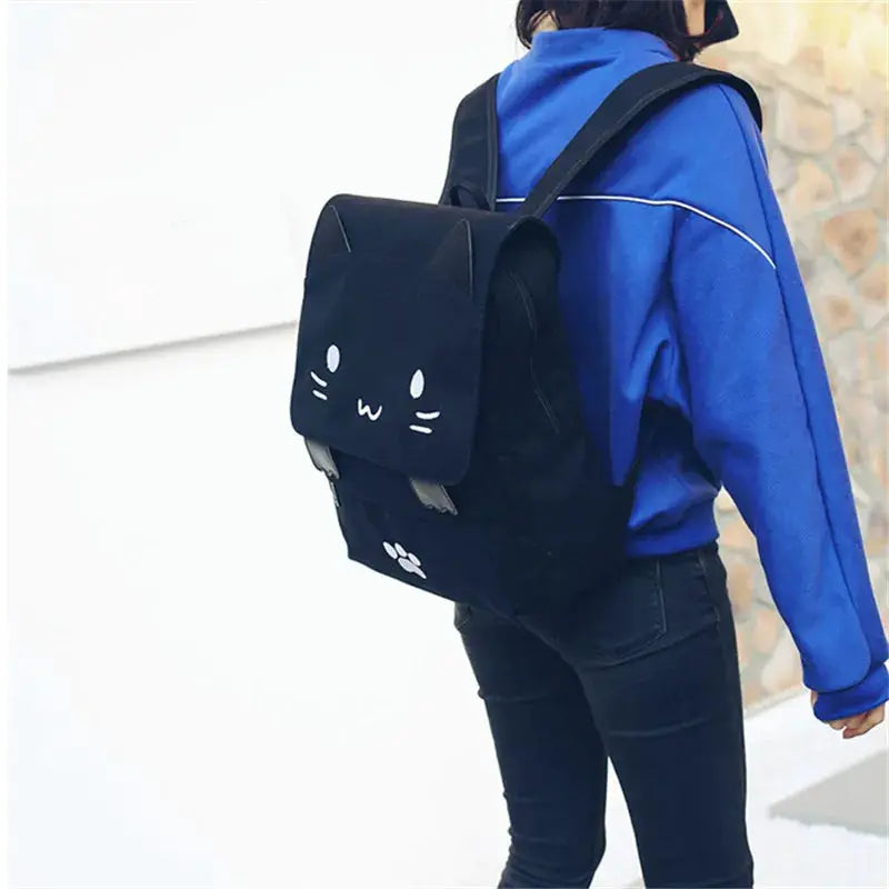 3D cat-face backpack, black large-capacity book bag with cat-ear flap, worn by a woman in a blue jacket.
