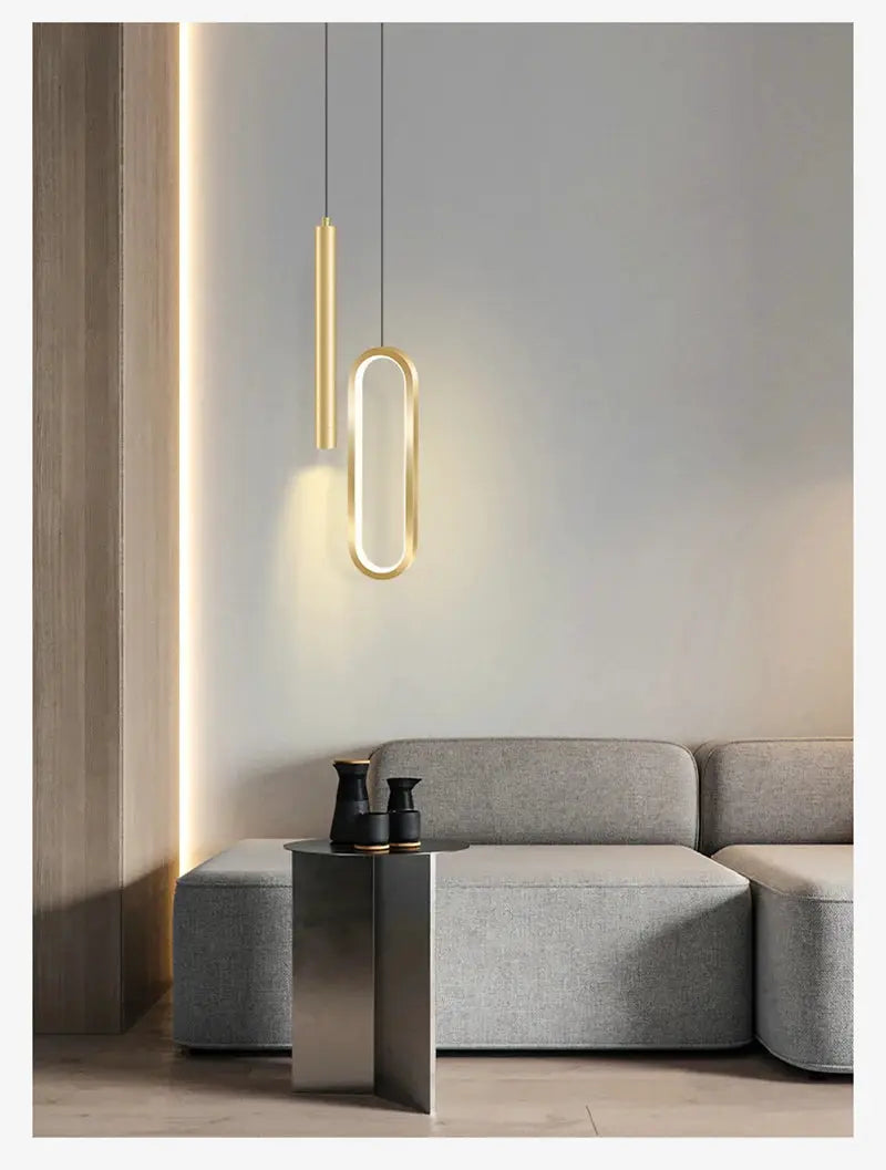 Two Nordic LED pendant lights, the oval loop and slim gold rod, hang over a gray sofa.
