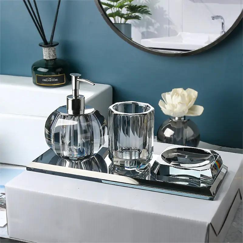 Three-piece glass bathroom set by Simples Market with clear lotion dispenser, tumbler, and soap dish on a mirrored tray