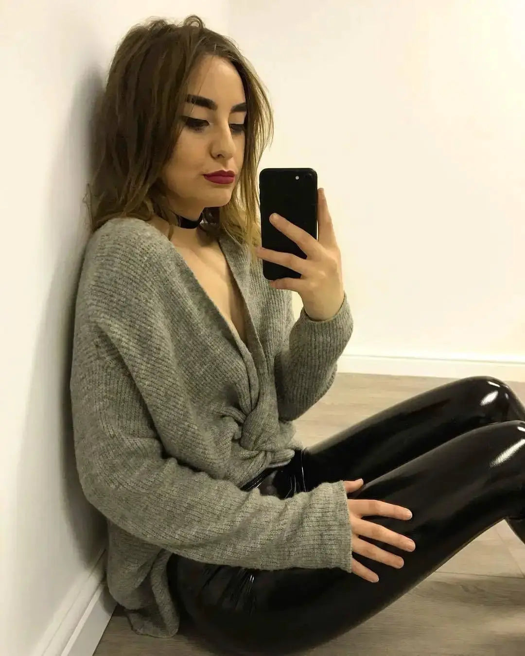 PU pants, black slim leather leggings; model sits on the floor in a gray knit cardigan, taking a mirror selfie.