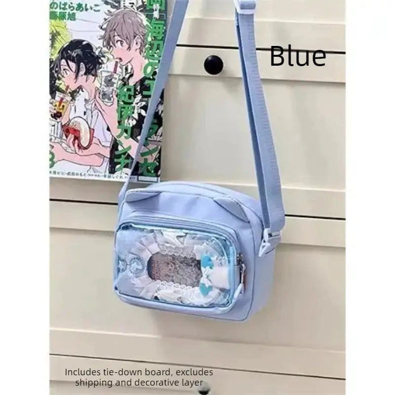 Blue ita bag with transparent front pocket, adjustable crossbody strap, lace trim, and badge display area.