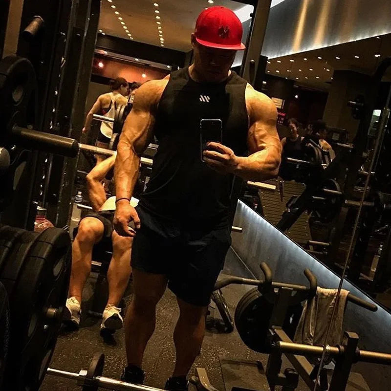Black men's bodybuilding tank top worn by a muscular man taking a mirror selfie in the gym