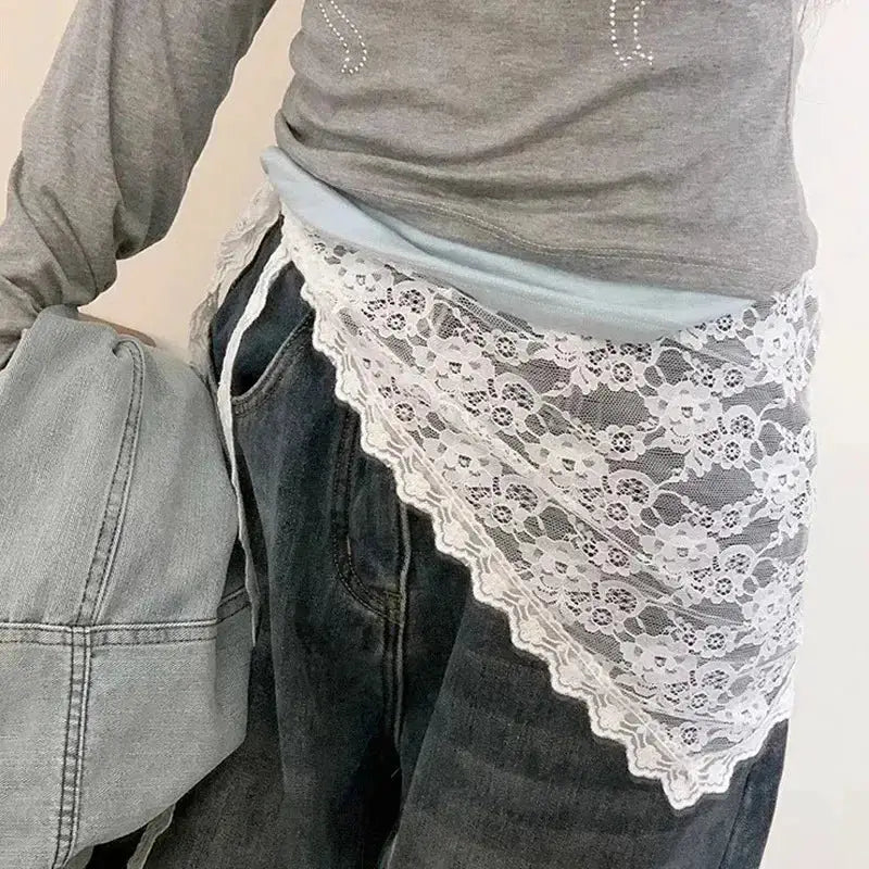 Women's lace mini skirt overlay with white floral lace, high-waist wrap style worn over denim jeans