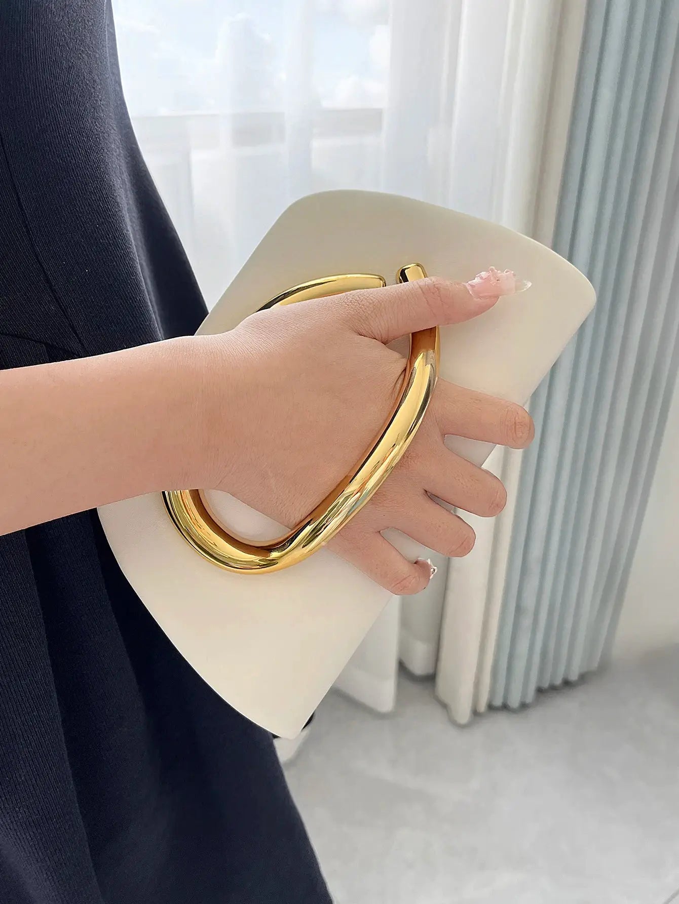 White box clutch with a bold gold-tone loop handle, held by a model in black attire