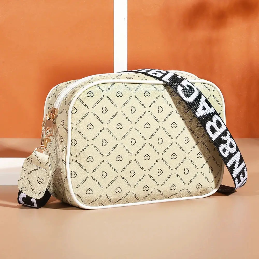 Beige crossbody bag with white piping and repeating logo pattern; adjustable black-and-white strap.