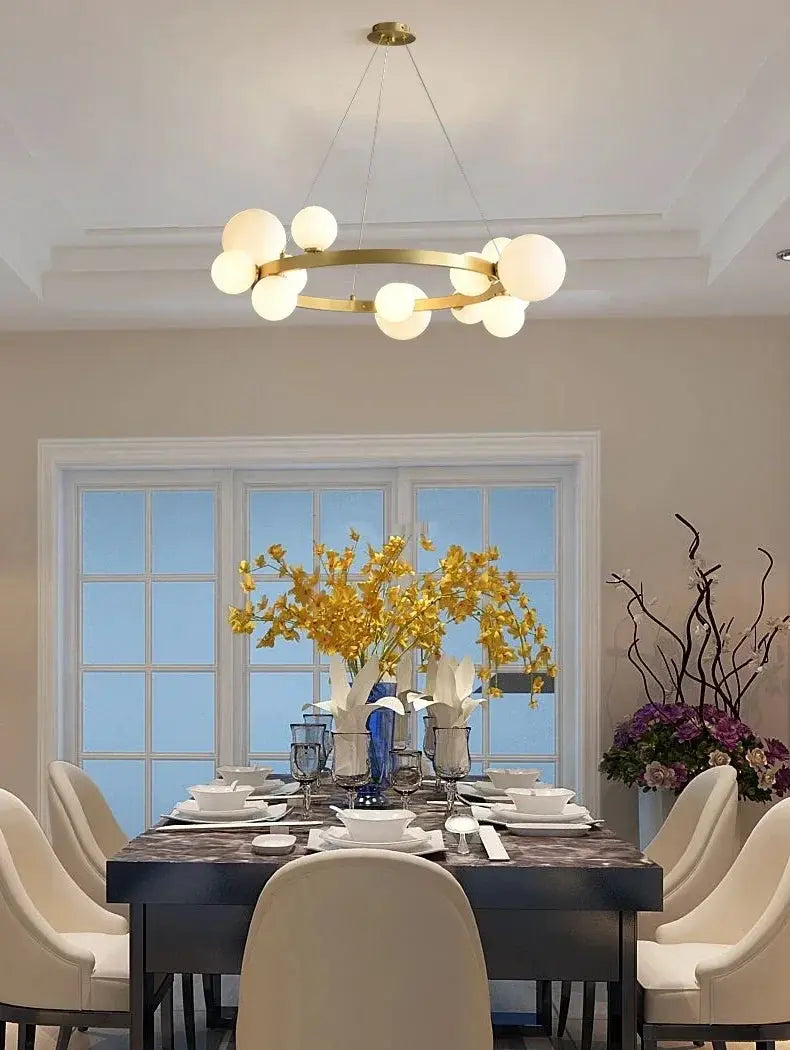 Simple chandelier by Simples Market, gold circular hanging lamp with frosted globe bulbs over a dining table.