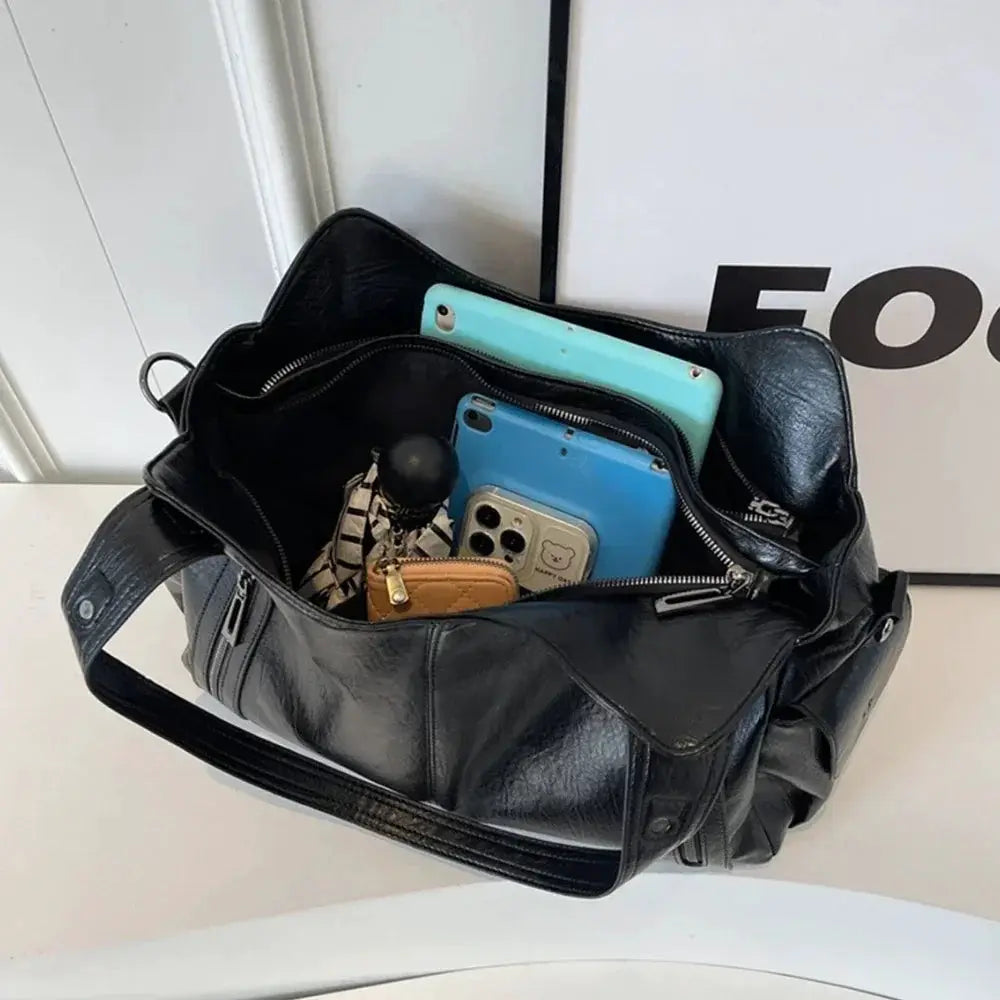 Soft interior compartment shoulder bag, black leather with zip pockets, holding blue and turquoise phones.