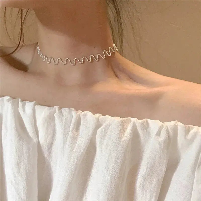 Beaded choker necklace with silver-tone crystals in a wavy design, worn on a white off-shoulder top