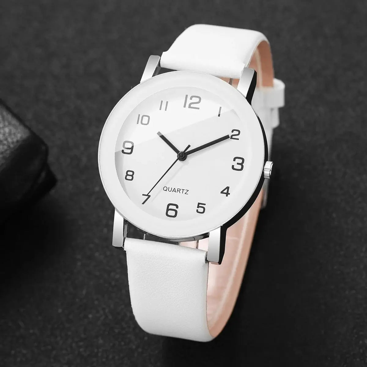 White leather strap wristwatch with silver case, black Arabic numerals on a white dial, quartz movement.