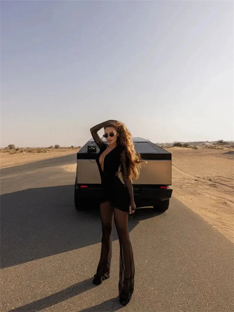 Jumpsuit, black deep-V neck long-sleeve see-through with ruched, sheer leg panels, model posing beside desert road SUV