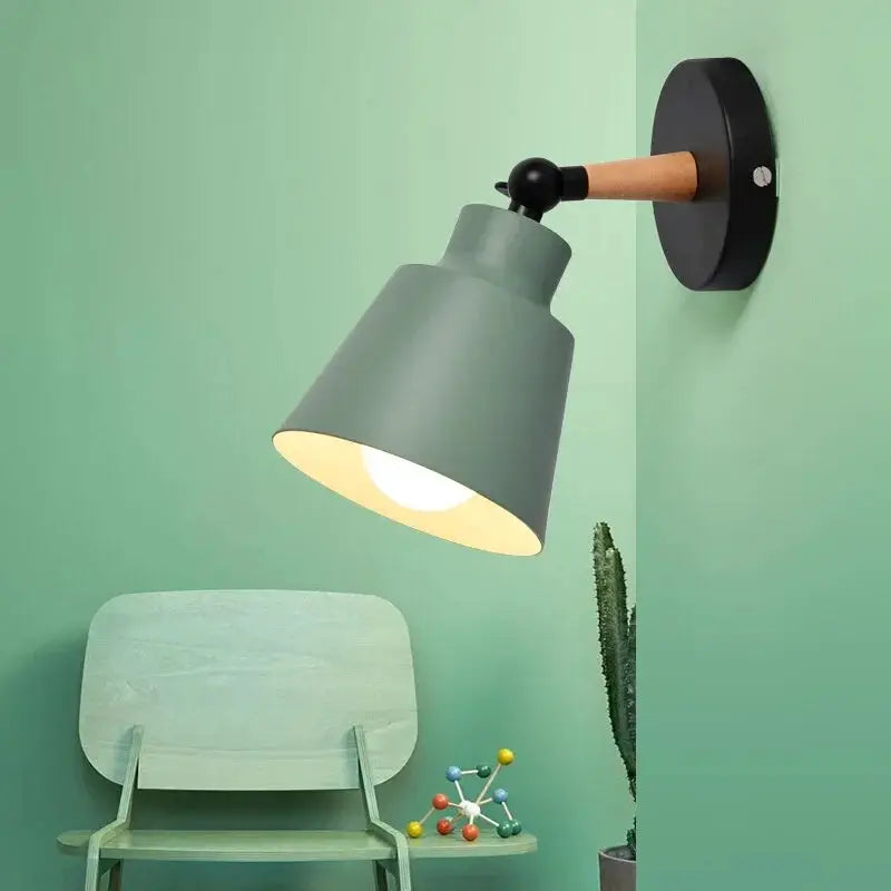 Nordic solid wood LED wall lamp with grey-green metal shade and wooden arm on black round mount, with chair and plant