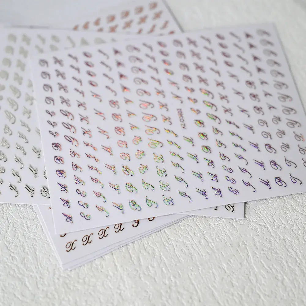 3 sheets of 3D Roman letter nail stickers by Simples Market; metallic gold/silver/black with holographic finish.