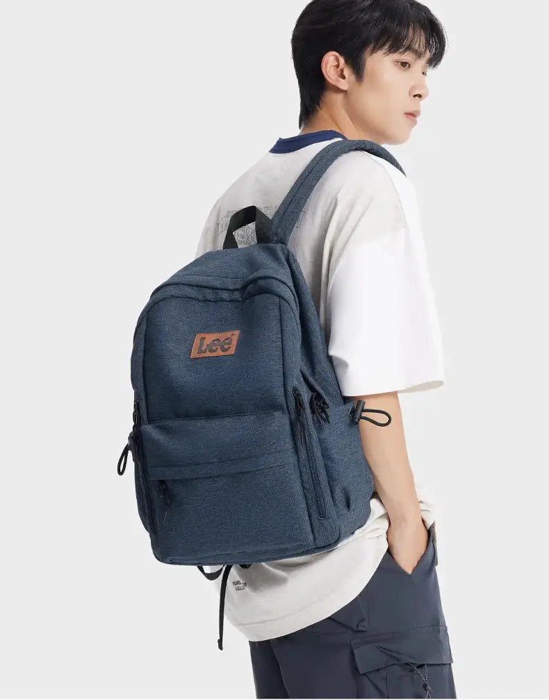 Lee 16-inch laptop backpack in blue denim with brown logo patch and multiple pockets carried by a man.