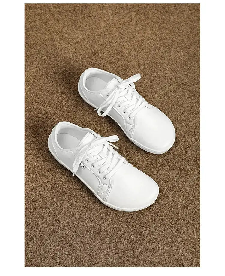 Pair of white lace-up sneakers on brown carpet, casual walking shoes.