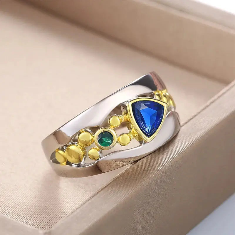 Huitan two-tone ring with a blue triangular CZ and green accent stone on a silver band with gold-tone detailing