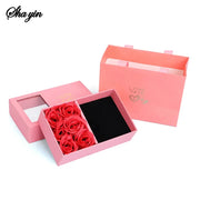 Pink jewelry box with red preserved roses and a black velvet insert; includes a matching pink gift bag.