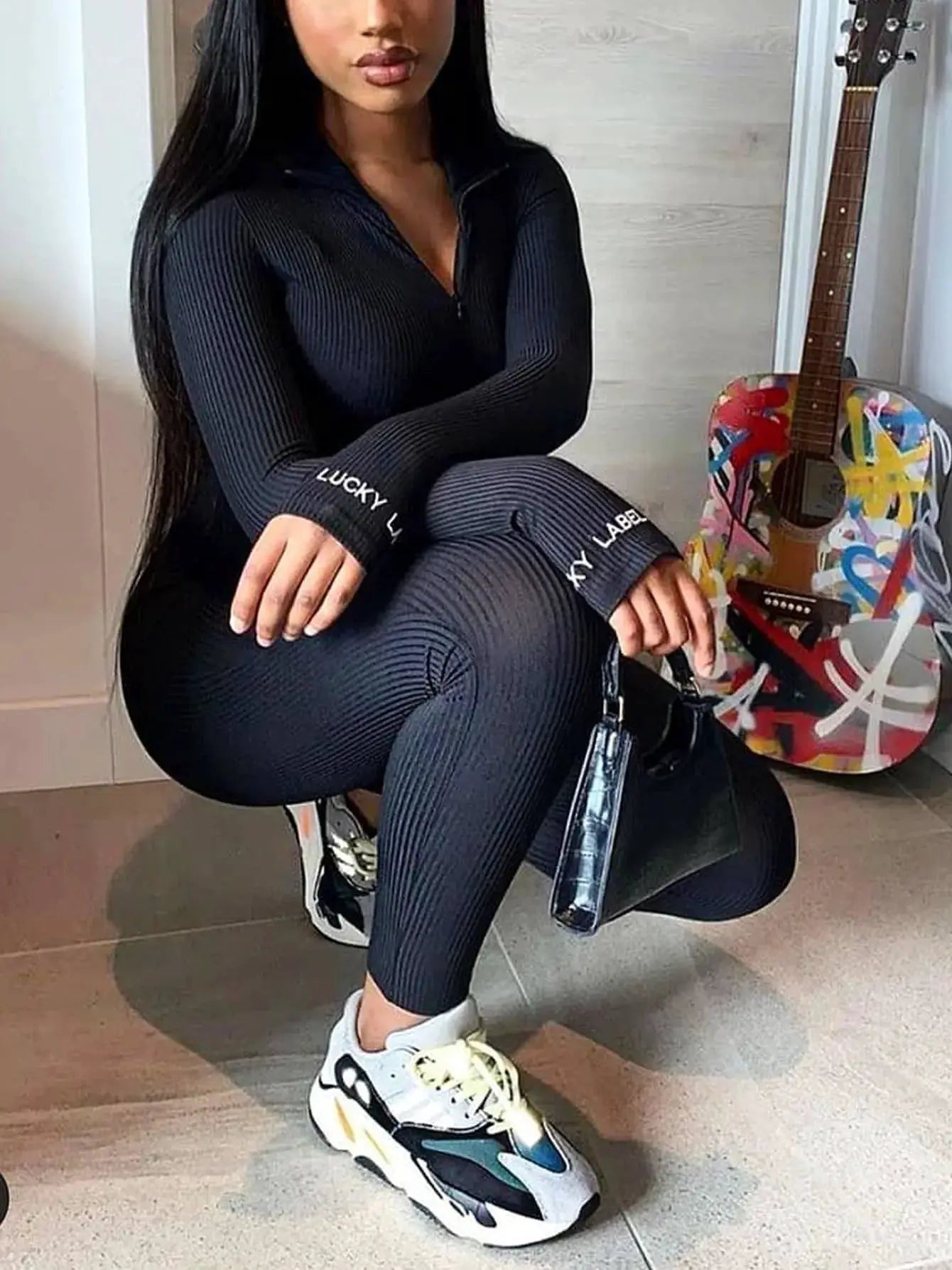 Black ribbed knit long-sleeve jumpsuit; form-fitting streetwear with Lucky Label text on cuffs.