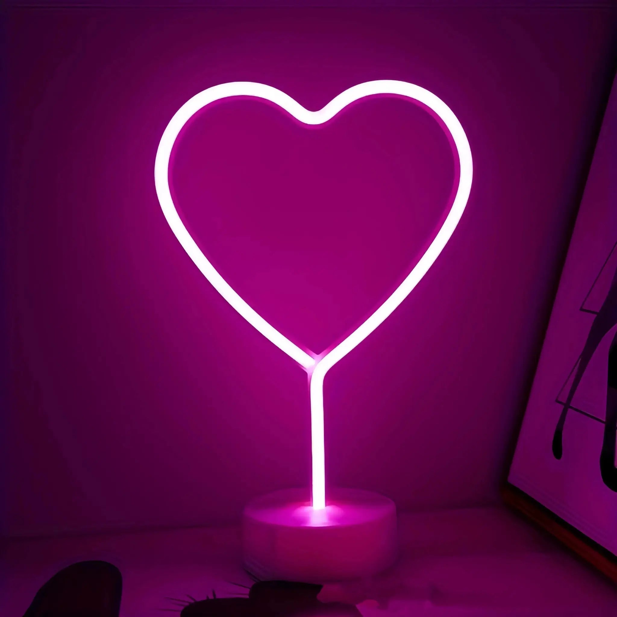 Heart-shaped neon light by Simples Market, pink glow, battery or USB powered, sits on a round base