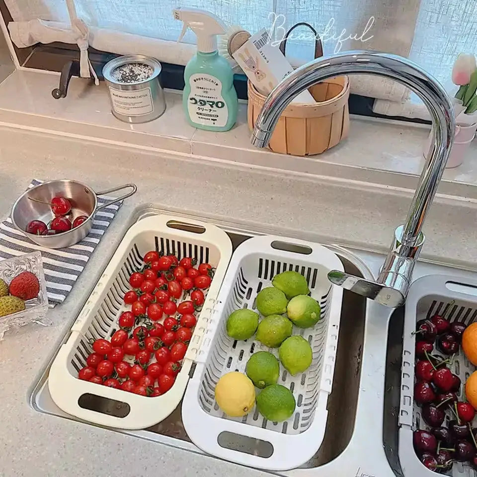 Three white plastic retractable kitchen sink drain baskets placed in a stainless sink, filled with tomatoes and limes.