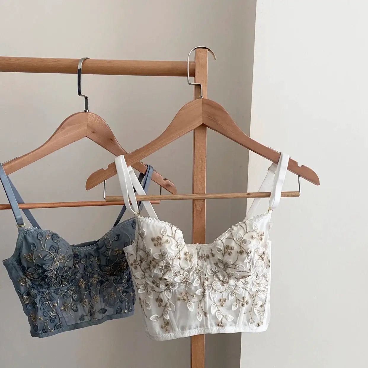 Two Simples Market embroidered bralettes on wooden hangers, blue and white floral lace with straps