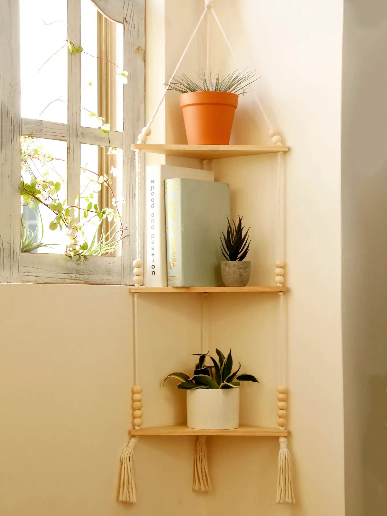 Wooden three-tier triangle corner floating shelf with rope hangers and tassels, displaying potted plants and books.