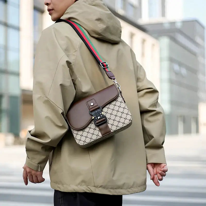 Crossbody bag with beige jacquard pattern and brown leather flap; green-red-green adjustable strap.