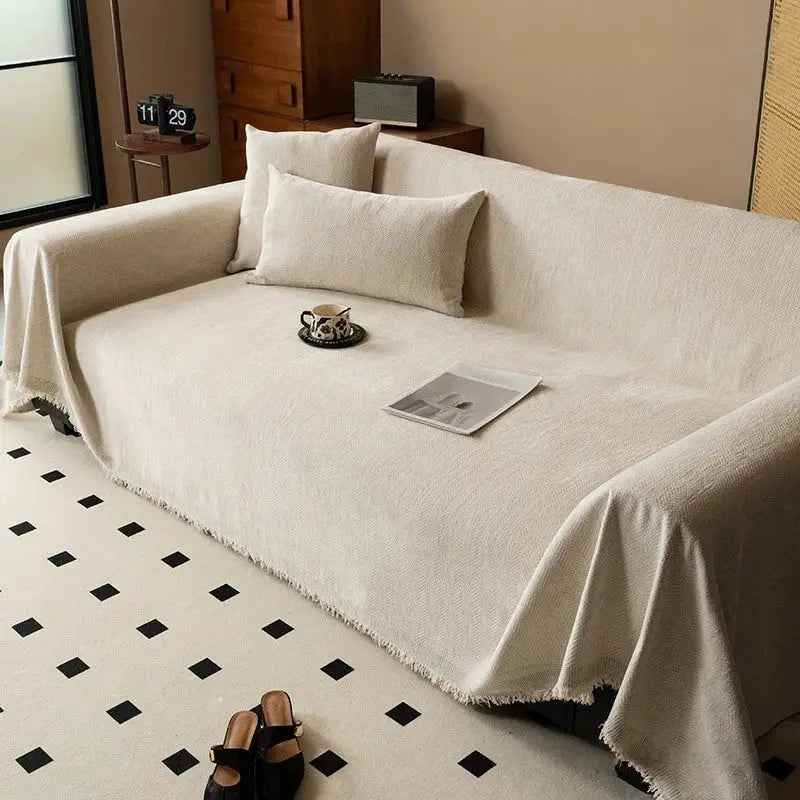Chenille sofa towel by Simples Market in cream with tassel edge, draped over a beige sofa.