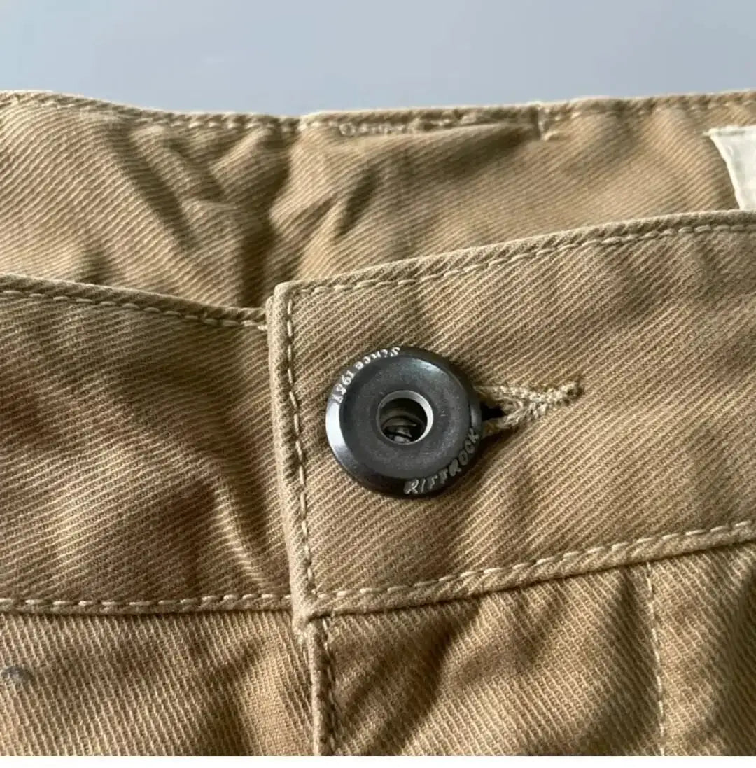 Cargo pants waistband in khaki cotton with black metal button and visible stitching