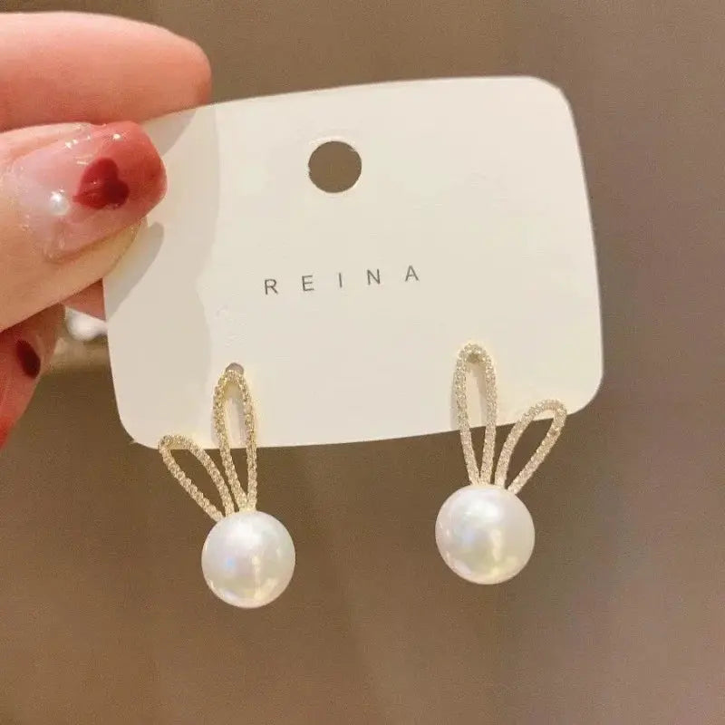 Pearl drop dangle earrings with gold-tone looped bow accents; white pearls on Reina card