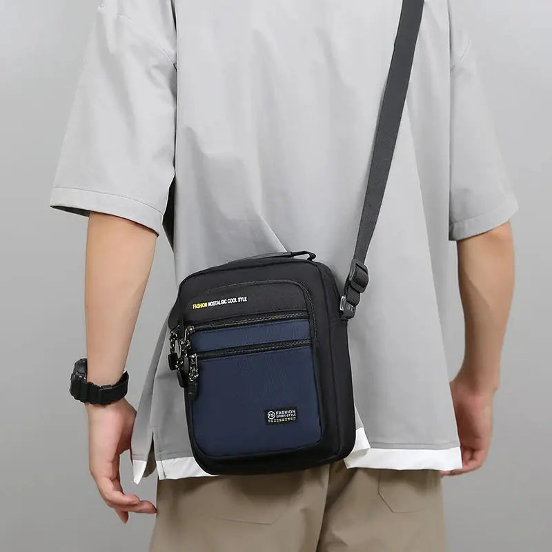 Simples Market men's Oxford crossbody bag with black body and navy front pocket, multiple zip pockets