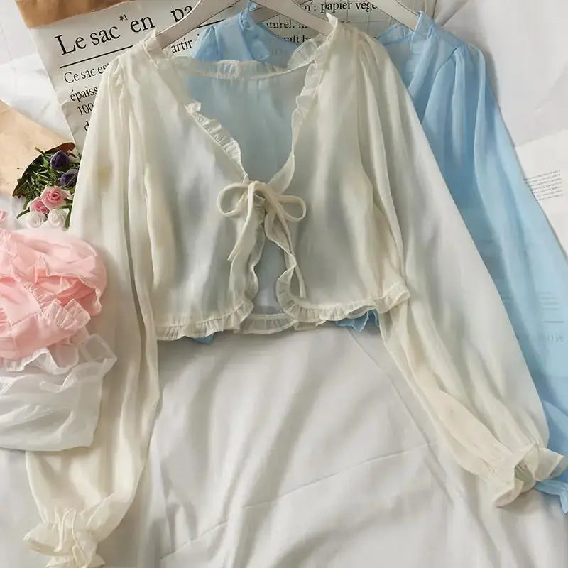 Two long-sleeve sheer lace bow-cardigans in white and light blue with ruffle trim and tie by Simples Market