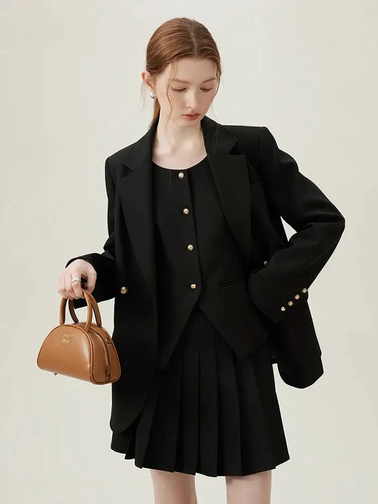 FSLE women's black blazer suit set with gold buttons and matching pleated skirt, model carries tan mini handbag