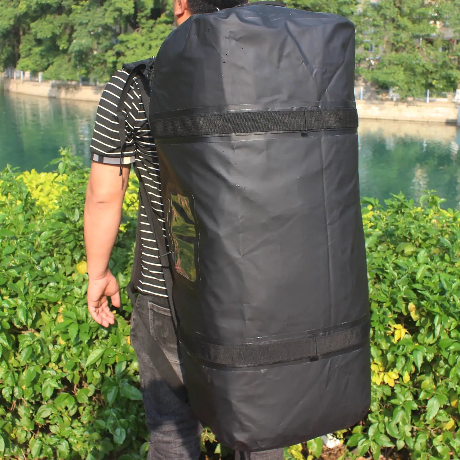 Black waterproof duffle bag (40–120L) strapped to a man's back outdoors