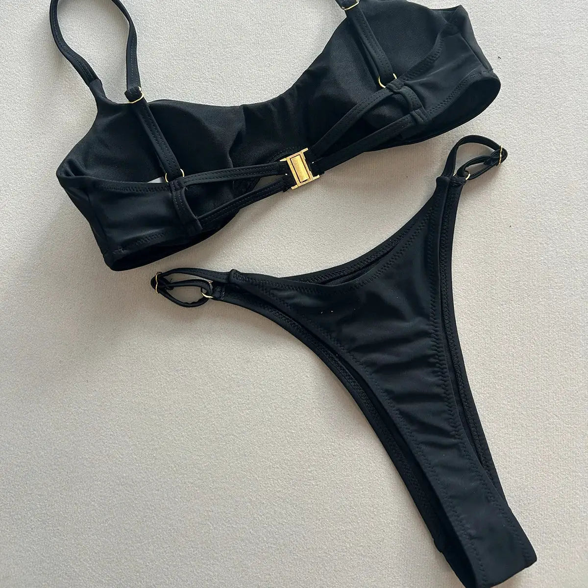 Simples Market black two-piece push-up bikini set with adjustable straps, gold hardware, thong bottom.