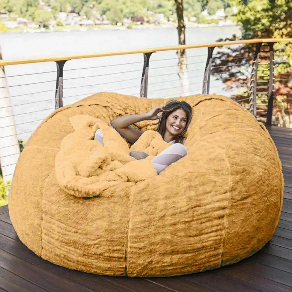 Giant tan fuzzy bean bag sofa bed on an outdoor deck with a smiling woman inside