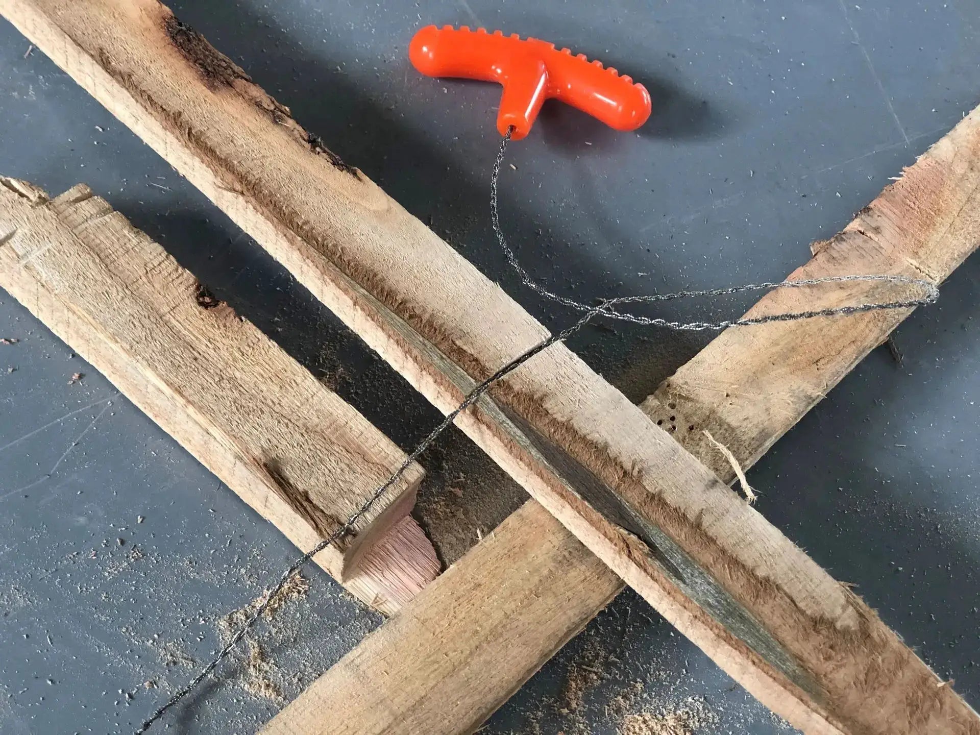 Manual rope chain saw with red plastic handle and twisted steel wire blade on wooden boards