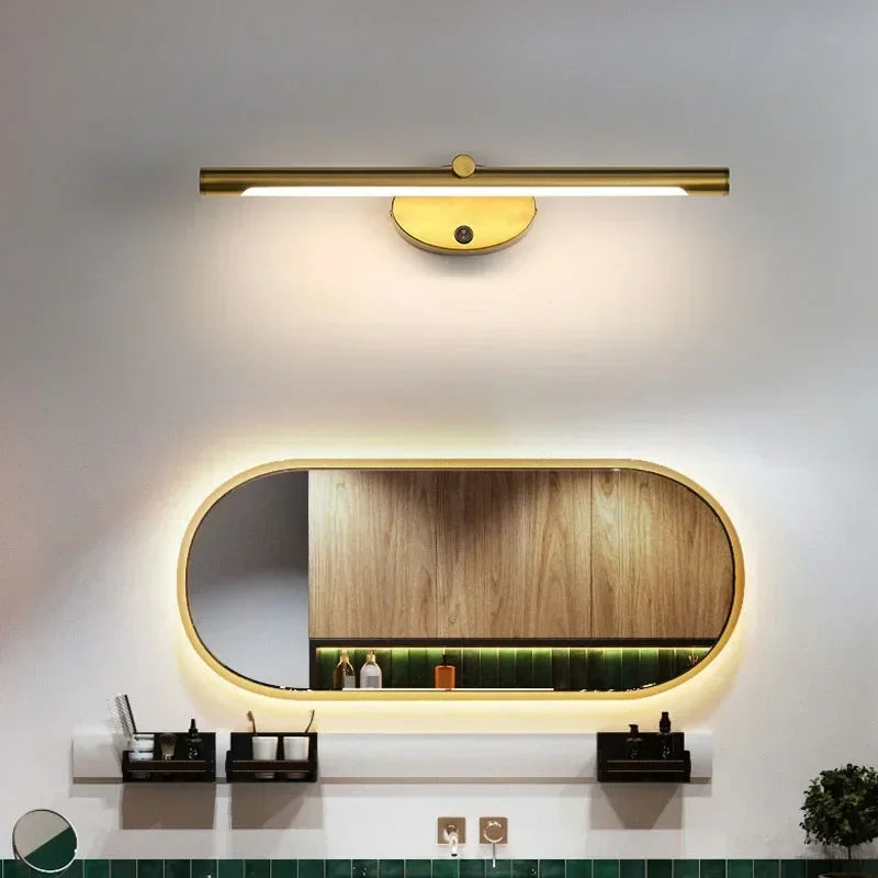Modern LED wall lamp in brass finish with touch switch, above oval backlit bathroom mirror