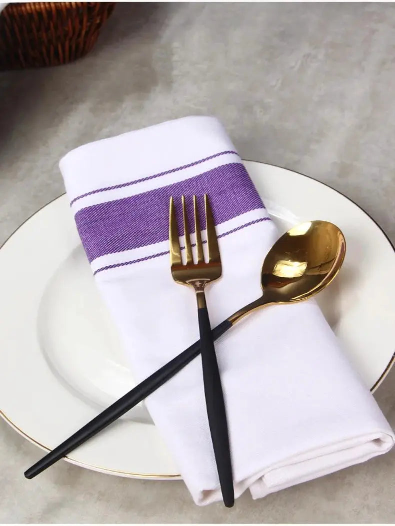 European kitchen towel placemat in white cotton with a purple stripe, paired with a black-handled fork and gold spoon on a white plate.