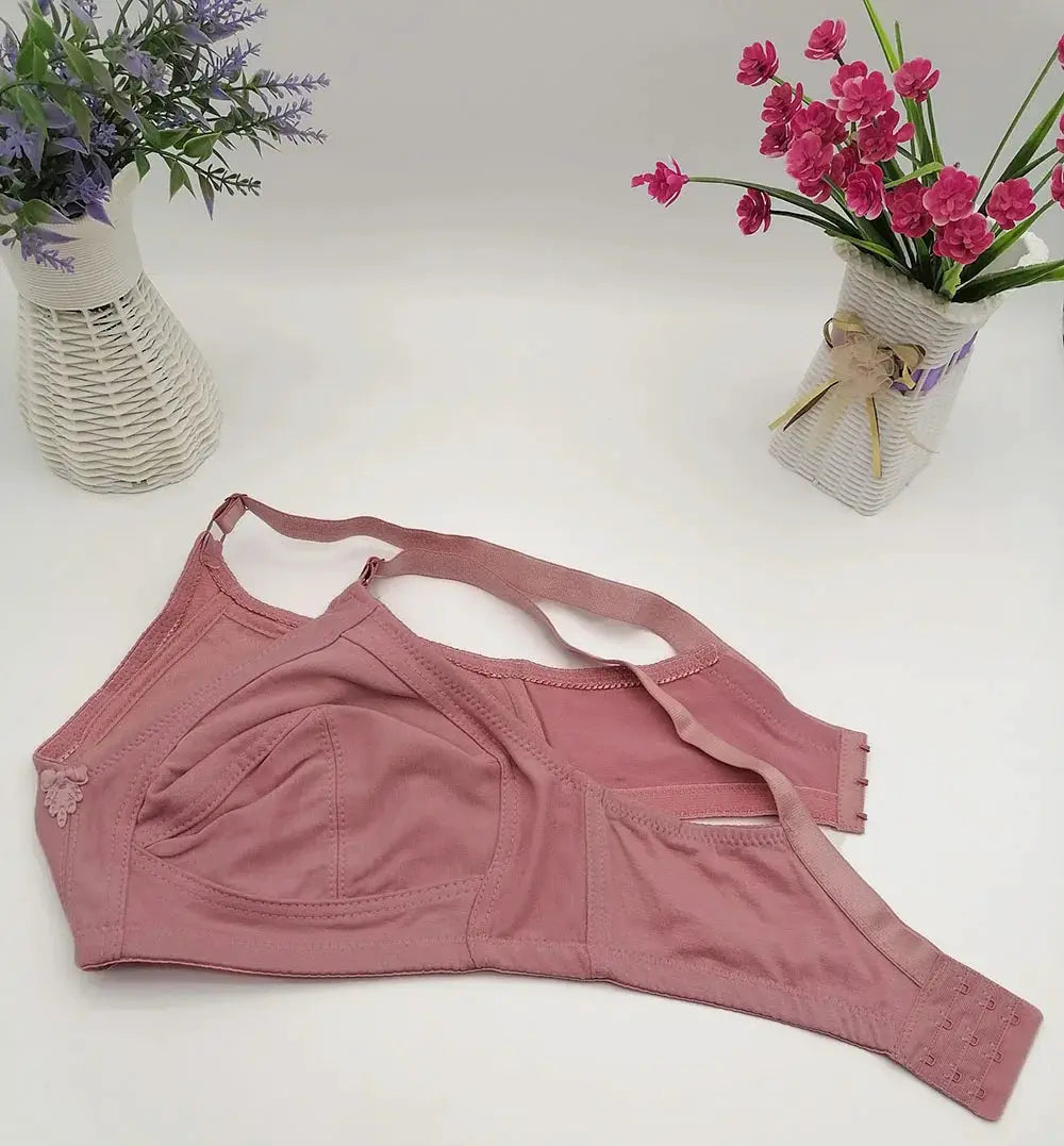 Pink plus-size bra with adjustable straps and back closure, cup seams, and small floral embellishment on the left cup